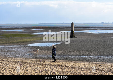 Dog walker goduto il soleggiato ma freddo tra la bufera di neve passando il Crowstone a Chalkwell nell'estuario del Tamigi. La bassa marea Foto Stock