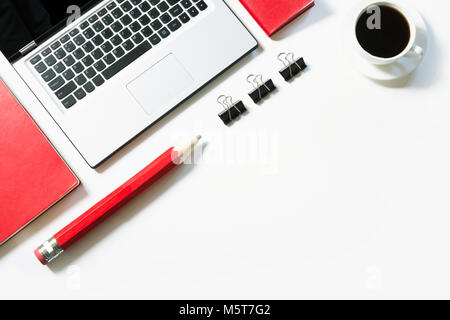 Postazione di lavoro con computer portatile, una tazza di caffè e accessori di colore rosso su sfondo bianco. Vista da sopra con copia spazio. Foto Stock