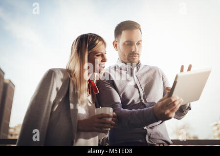 Colleghi di lavoro avente pausa caffè e con tavoletta digitale sul balcone di fronte all'ufficio. Foto Stock