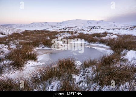 Nevoso inverno mattina nelle colline del Peak District. Un pool di congelati a sud di testa, Hayfield con vista al Kinder Scout. Foto Stock