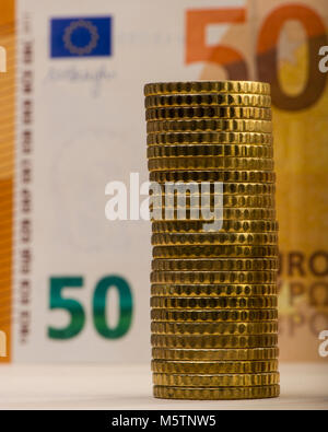 Pila di monete metalliche ripiegate sullo sfondo di una carta sbiadita bill di cinquanta euro. Euro denaro. Cambio dell'Unione europea. Foto Stock