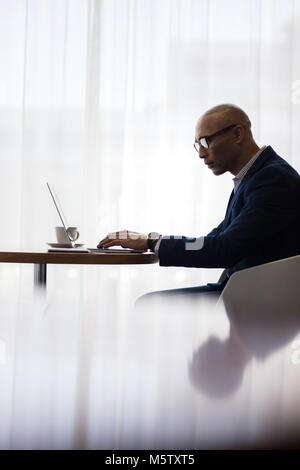 Maschio di lavoratore di ufficio utilizzando il portatile in ufficio. Vista laterale del business uomo seduto a tavola e di lavoro sul computer portatile. Foto Stock