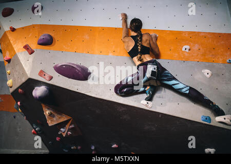 Athletic donna bouldering in una piscina centro di arrampicata. Alpinista professionista praticare arrampicate su roccia in una piscina palestra di arrampicata. Foto Stock