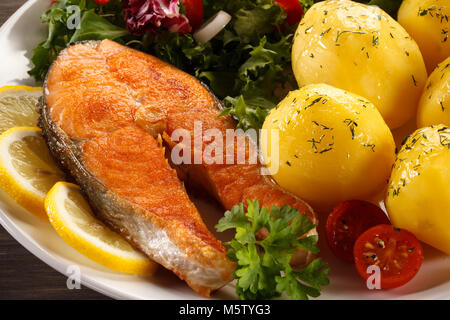 Salmone fritto e verdure sul tavolo di legno Foto Stock