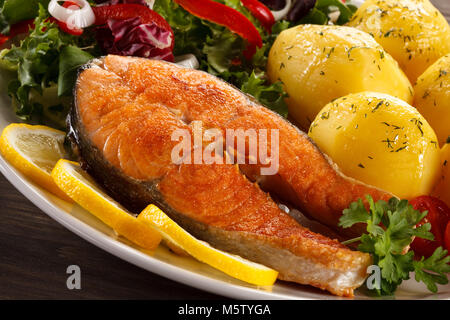 Salmone fritto e verdure sul tavolo di legno Foto Stock