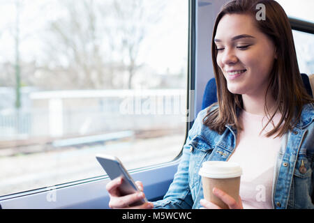 Giovane donna sms sul cellulare durante il viaggio in treno Foto Stock