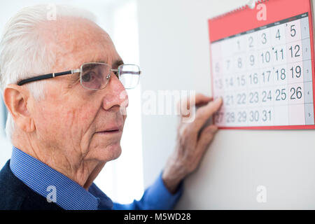 Confuso uomo anziano con demenza guardando il calendario da parete Foto Stock