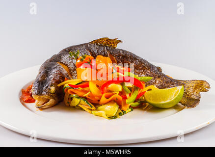 Trota grigliata intera con verdure arrostite e salsa di pomodoro servita su un elegante piatto del ristorante. Foto Stock