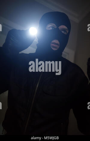 Ladro che indossa una maschera con una torcia in casa. Foto Stock