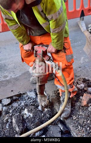 Workman foro di scavo in strada con martello da demolizione per rompere la superficie, REGNO UNITO Foto Stock