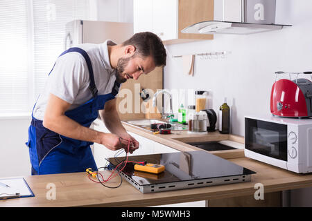 Tecnico maschio riparazione Fornelli a induzione con multimetro digitale in cucina Foto Stock