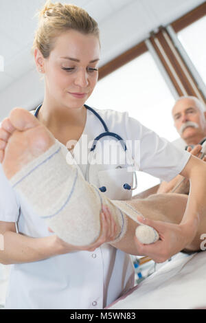 Medico donna del bendaggio gamba del paziente in ospedale Foto Stock