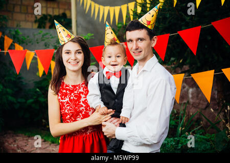 Tema bambini festa di compleanno. Padre di famiglia e madre figlio di contenimento di un anno sullo sfondo di verde e di decorazioni festive, ghirlande e colorato Foto Stock