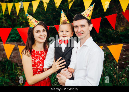 Tema bambini festa di compleanno. Padre di famiglia e madre figlio di contenimento di un anno sullo sfondo di verde e di decorazioni festive, ghirlande e colorato Foto Stock