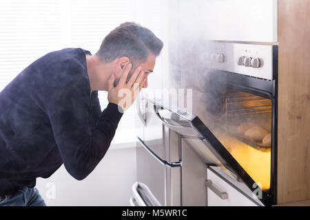 Scioccato uomo Guardando bruciò i cookie con i fumi provenienti dal forno Foto Stock