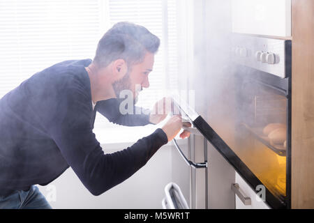 Scioccato uomo Guardando bruciò i cookie con i fumi provenienti dal forno Foto Stock