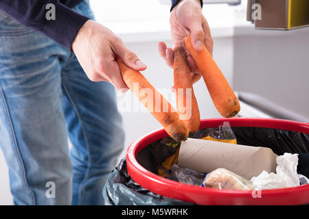 Close-up di mano di una persona gettando carota nel bidone della spazzatura Foto Stock
