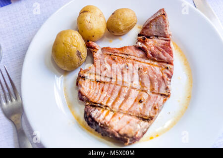 Succosa bistecca di tonno con patate servita su piastra bianca Foto Stock