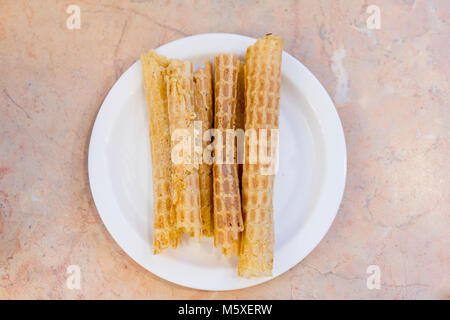 Bella dolce tubi di wafer dalla pasta sottile giacciano in fila. Gustosa pasta cotta su piastra ceramica. Foto Stock