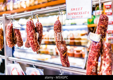 Primo piano della sopressata e Genova rulli salami appesi a ganci di stringa di visualizzazione in un mercato negozio di macellaio, prezzo per libbra Foto Stock