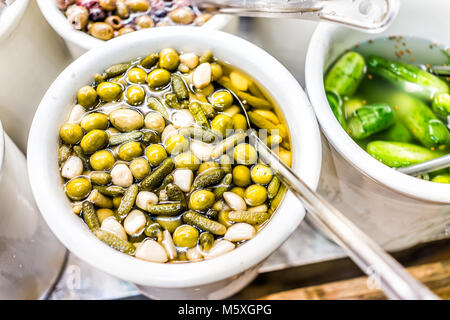 Vista dettagliata del contenitore in plastica vaso riempito con il bulk green sottaceti cetriolini, aglio, olive, cornichon in salamoia di aceto Foto Stock