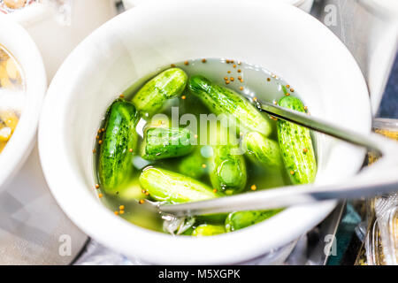 Vista dettagliata del contenitore in plastica vaso riempito con il bulk metà verde sour sottaceti, semi di senape in salamoia di aceto Foto Stock