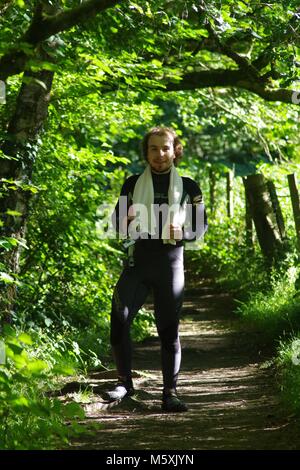 Bel giovane in muta con un asciugamano in posa su un sentiero di bosco sotto il fogliame vibrante, prima di Wild nuotare nel fiume Dart, South Devon, Regno Unito. Foto Stock