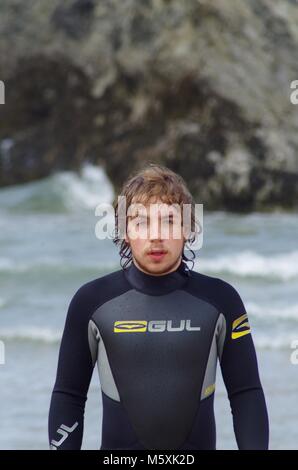 Giovani, resistente bello British Surfer, in una muta sulla spiaggia di Holywell, North Cornwall, Regno Unito. Surf Lifestyle. Foto Stock