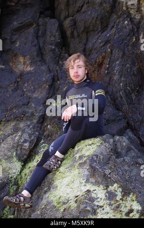 Giovani, resistente bello British Surfer, in una muta sulla spiaggia di Holywell, North Cornwall, Regno Unito. Surf Lifestyle. Foto Stock