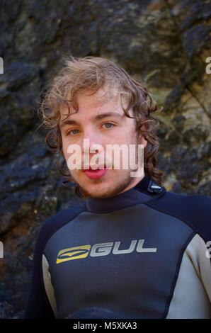 Giovani, resistente bello British Surfer, in una muta sulla spiaggia di Holywell, North Cornwall, Regno Unito. Surf Lifestyle. Foto Stock