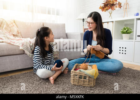 Sweet Asian kids stay con sua madre e godere di maglia insieme seduta sul pavimento del salotto di casa Foto Stock