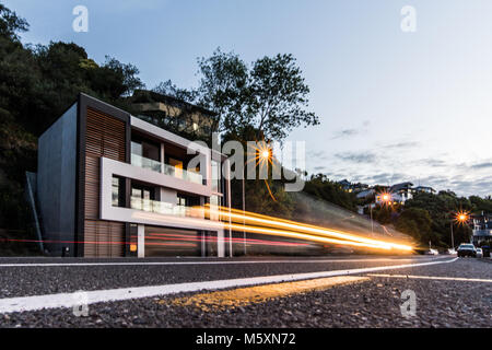 Auto accelerando da al crepuscolo, la luce sentieri, casa moderna e quartiere in background Foto Stock