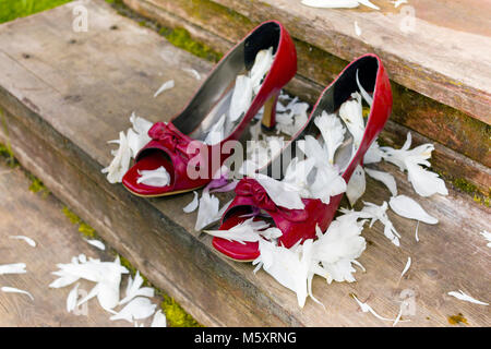 Rosso scarpe matrimonio con petali di rosa intorno al posto sulla casa in legno passi, outdoor closeup Foto Stock