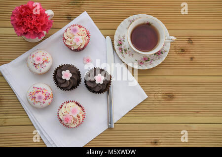 Deliziosi cibi fatti in casa di piccoli dolci e tazza di tè con fiori Foto Stock