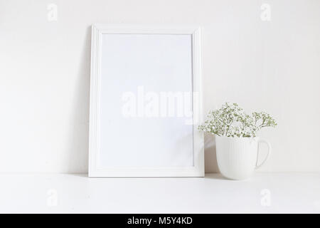 Vuoto bianco telaio in legno mockup con baby soffio, Gypsophila fiori nella tazza di porcellana sul tavolo. Poster design di prodotto. Stile femminile stock photography. Home decor. Foto Stock