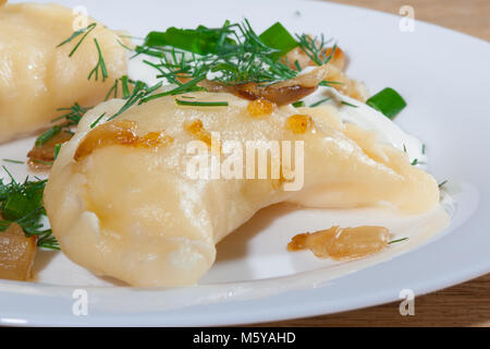 Vareniki ucraini servita sulla piastra Faror con cipolle, panna acida e aneto Foto Stock