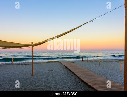 New Scenic 5 posti a colori del tramonto sul mare in una spiaggia sabbiosa del Mar Mediterraneo con un ponte di legno,percorso verso l'oceano e da un telo di grandi dimensioni Foto Stock