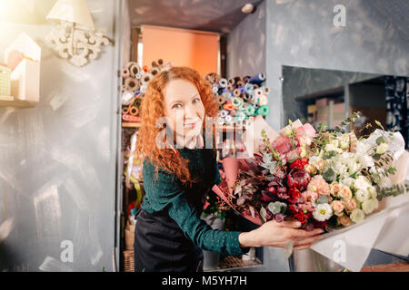 Happy shop assistant che mostra preparato ricco bouquet floreale in negozio Foto Stock