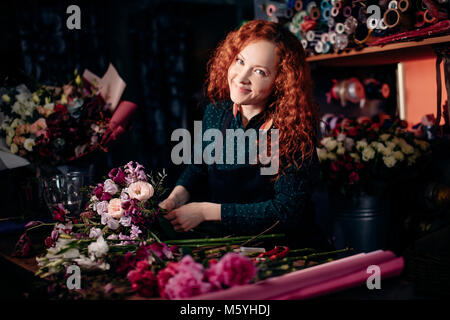 Lo zenzero donna in piedi a tavola e rendere la composizione floreale al negozio di fiori Foto Stock