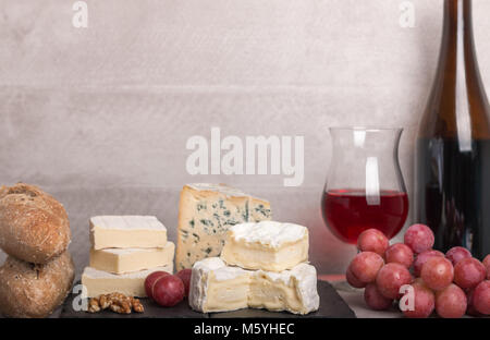 Il vino e il formaggio set. varietà di formaggio,l'uva,baguette,dadi su una scheda e un bicchiere di vino rosso e una bottiglia. Con il fuoco selettivo. Foto Stock