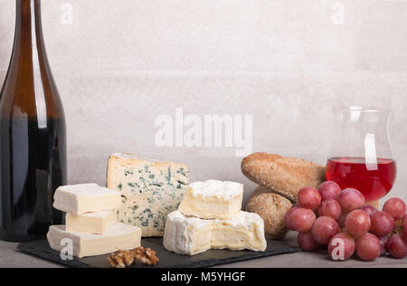 Il vino e il formaggio set. varietà di formaggio,l'uva,baguette,dadi su una scheda e un bicchiere di vino rosso e una bottiglia. Con il fuoco selettivo. Foto Stock