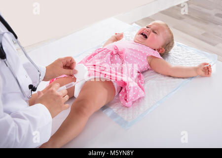 Medico dando iniezione di vaccino per piangere Bambina in clinica Foto Stock