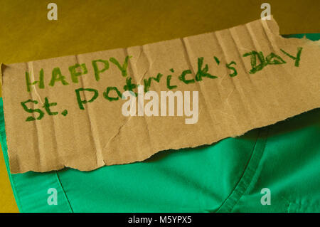 Il concetto di preparazione per la celebrazione della festa di San Patrizio, camicia verde si trova sul tavolo, testo, sfondo dorato Foto Stock