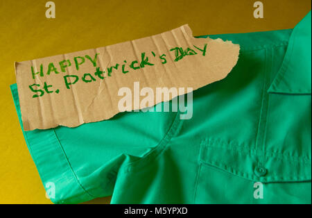 Il concetto di preparazione per la celebrazione della festa di San Patrizio, camicia verde si trova sul tavolo, testo, sfondo dorato Foto Stock