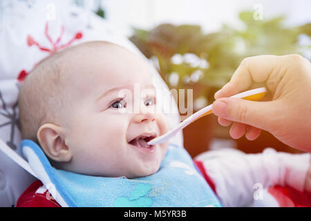 Un bambino mangiare con il cucchiaio a tavola. Felice ed emozionato. Foto Stock