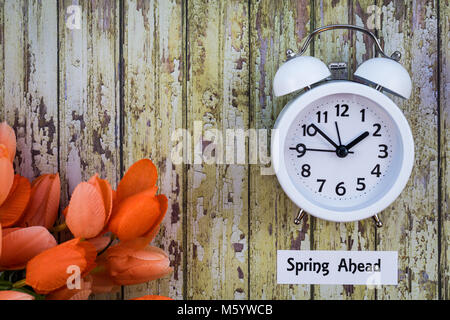 Ora legale davanti a molla concetto su tavola di legno, vista dall'alto in basso, con orologio bianco e tulipani Foto Stock