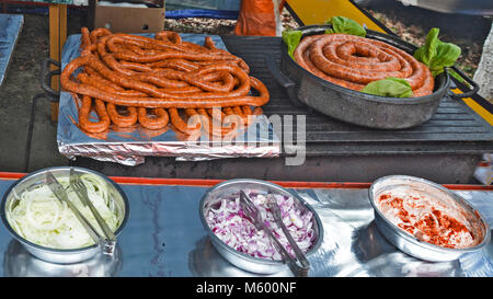 Salsicce fresche prodotte in attesa di grigliare e spezie sul tavolo. Foto Stock