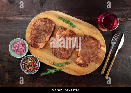 Una foto aerea di tre fette di carne cotta, filetti di manzo, ripresa dall'alto sul buio rustica con rametti di rosmarino, sale, pepe, vino, Foto Stock