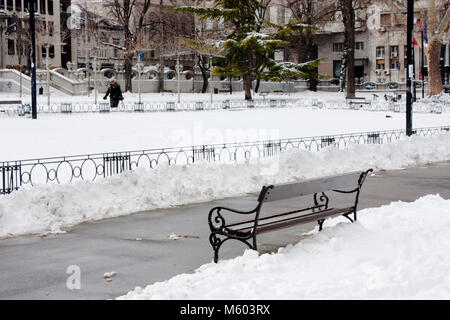 A Belgrado, in Serbia - Febbraio 27th, 2018: Centro parco coperto da neve, un banco vuoto e una donna in piedi la distanza Foto Stock