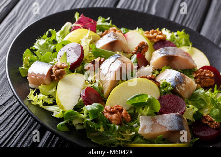 Preparate di fresco sgombro con insalata di mele, noci, barbabietole da zucchero e mescolare lattuga close-up su una piastra nera sul tavolo orizzontale. Foto Stock